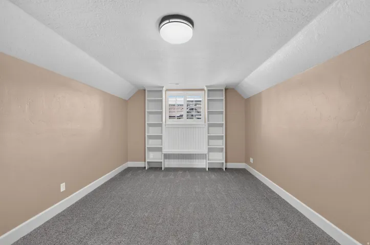 Built-in shelving, window with white blinds, beadboard wainscoting, textured walls, and flush-mount ceiling light