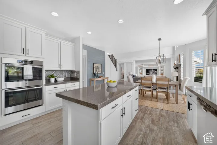 Gourmet kitchen featuring stainless steel double ovens, white shaker cabinetry, an island with stone countertops, and wood-finish flooring