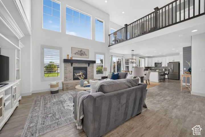 Vaulted ceilings with high windows, a fireplace with stone surround and mantle, built-in entertainment center, open-concept design, and wood-finish flooring