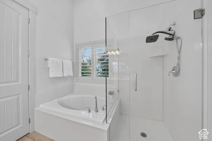 Glass-enclosed shower with a rainfall shower head, separate soaking tub with chrome fixtures, and window with plantation shutters