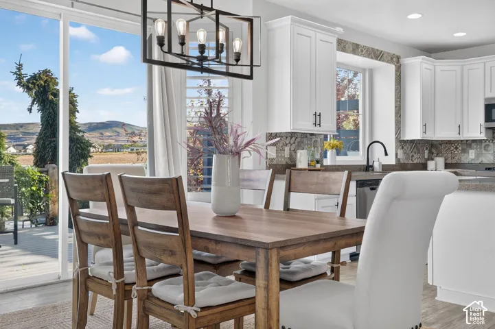 Modern geometric chandelier, white shaker cabinetry, patterned tile backsplash, stainless steel dishwasher, and sliding glass door