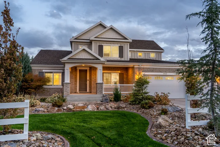 Multi-level exterior featuring brick and siding, a covered porch with white railings, an attached two-car garage, and a landscaped front yard with grass and rock features