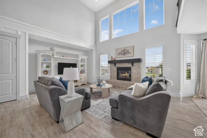 Vaulted ceiling with high transom windows, wood-finish flooring, brick fireplace with a dark wood mantel, built-in shelving, and plantation shutters