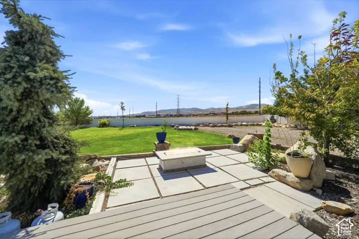 Expansive backyard featuring a manicured lawn, a stone paver patio, composite decking, and a built-in fire pit