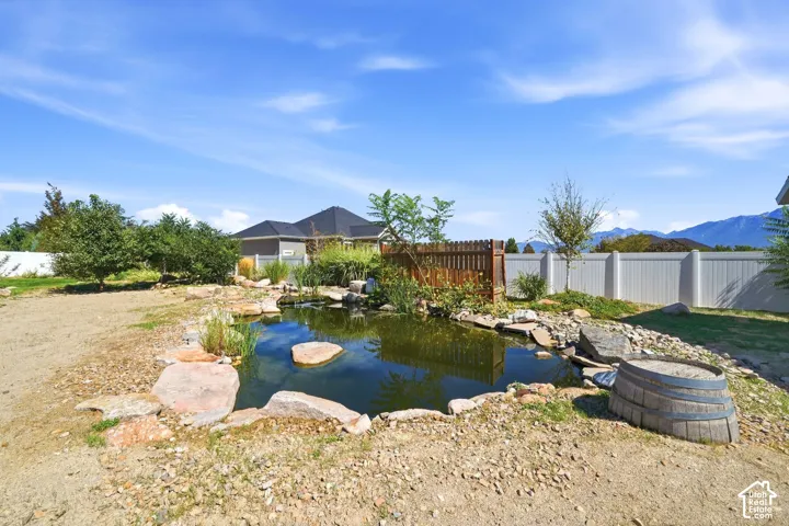 Backyard pond with natural rock accents, surrounded by landscaping, with a wood-fenced and vinyl-fenced perimeter
