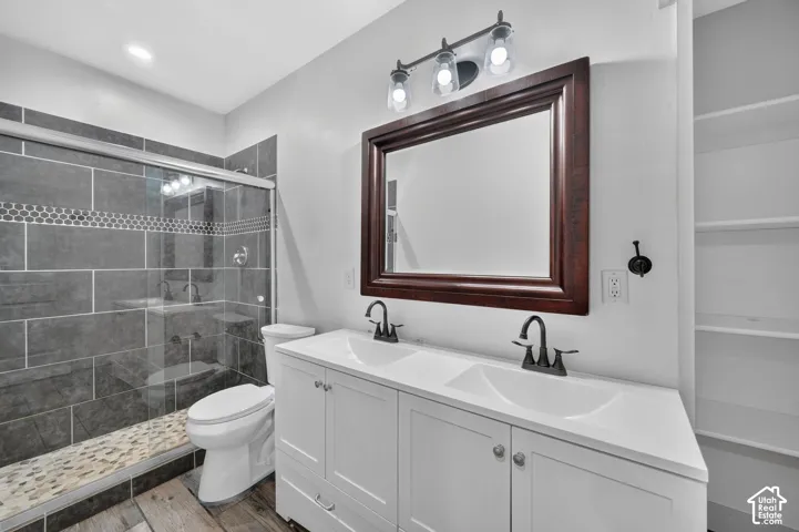 Dual basin vanity with white cabinetry, wood-finish flooring, and a glass-enclosed shower featuring large format tile and a pebble floor