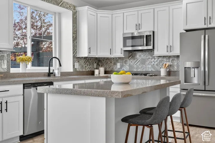 Kitchen featuring white shaker-style cabinetry, a built-in stainless steel microwave, a gas range with a patterned tile backsplash, and a large window above the sink with a matte black faucet