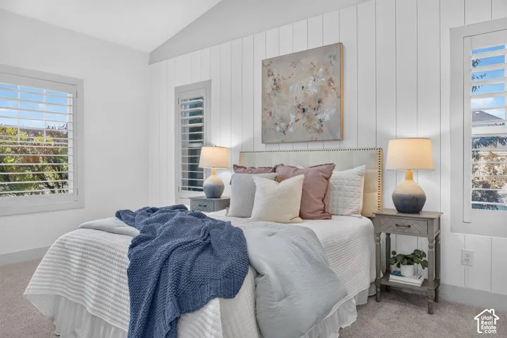 Vaulted ceiling, white shiplap accent wall, plantation shutters, and carpet flooring