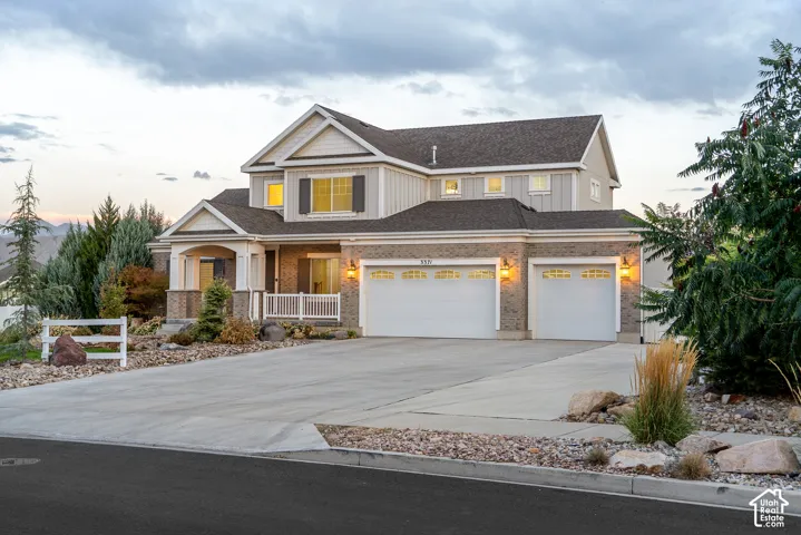 Expansive concrete driveway, attached three-car garage with carriage-style doors, covered front porch, brick and siding exterior, and established landscaping