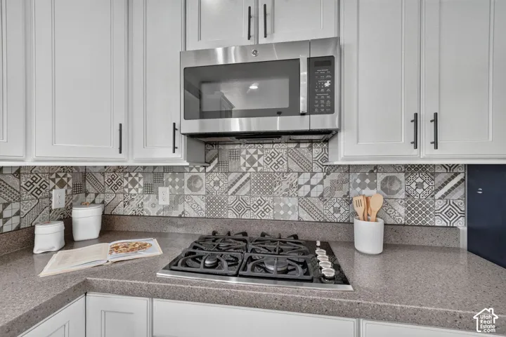 Stainless steel over-the-range microwave, gas cooktop, quartz-finish countertops, decorative tile backsplash, and white shaker-style cabinetry with matte black hardware