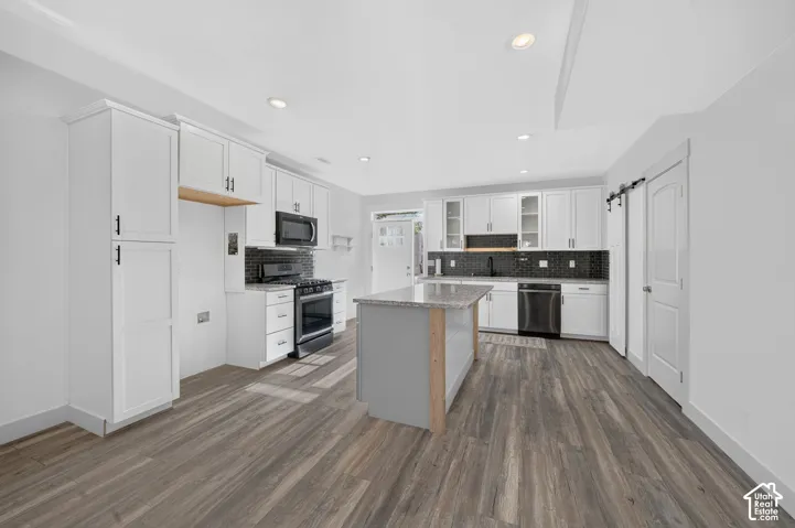 Modern kitchen featuring white cabinetry, dark tile backsplash, stainless steel appliances, a center island with a light-colored countertop, and wood-finish flooring