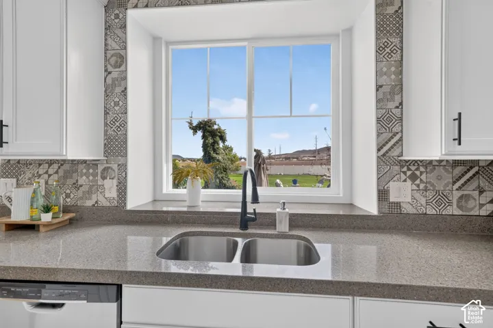 Stainless steel double-basin sink, quartz-finish countertop, patterned tile backsplash, white shaker-style cabinetry, and a modern black faucet