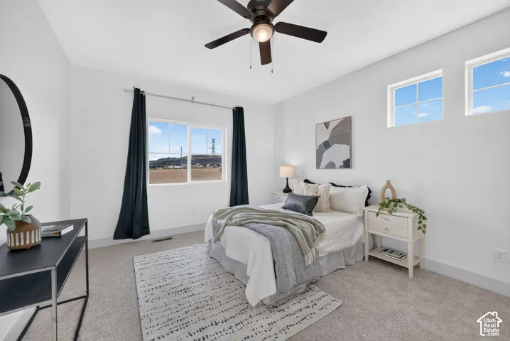 Carpeted flooring, white walls, multiple windows, and a ceiling fan with integrated lighting