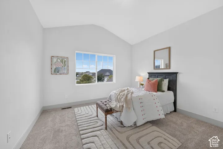 Vaulted ceiling, carpeted flooring, large window with grid pattern, neutral wall color, and dark headboard