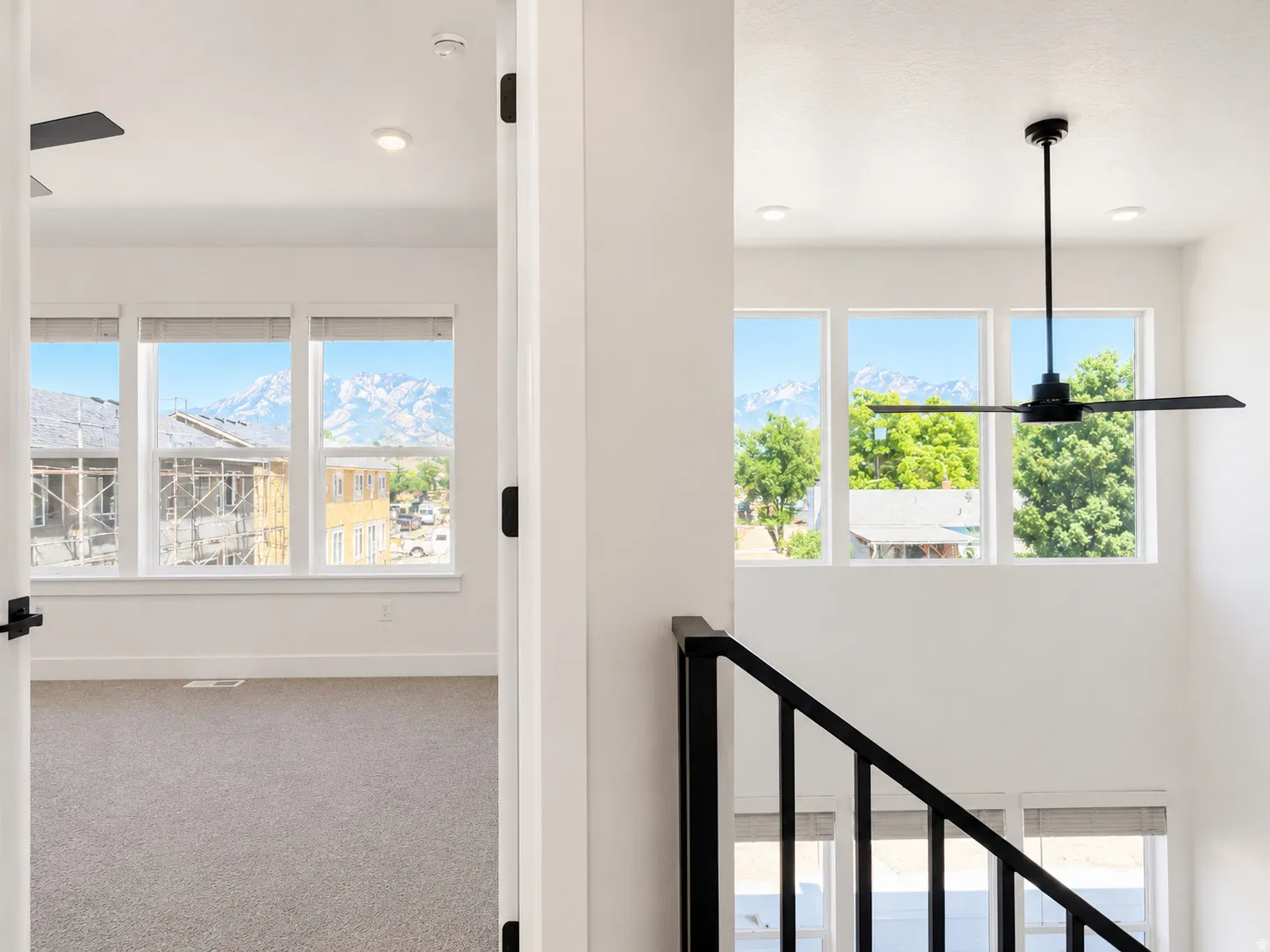Expansive windows with mountain scenery, black metal stair railing, high ceilings, recessed lighting, and a contemporary ceiling fan