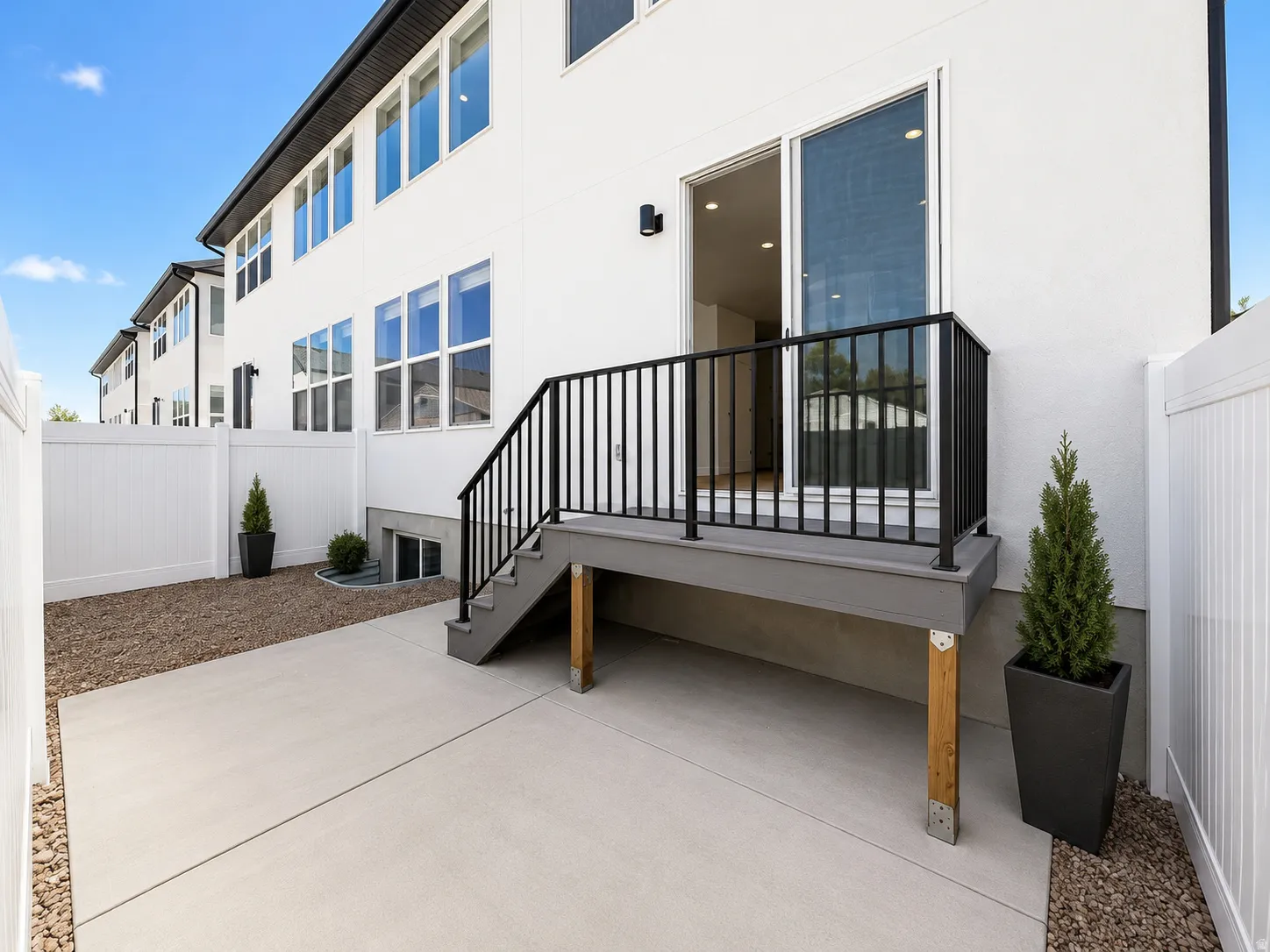 Ground-level concrete patio with a privacy fence and a staircase leading to an elevated deck with a sliding glass door