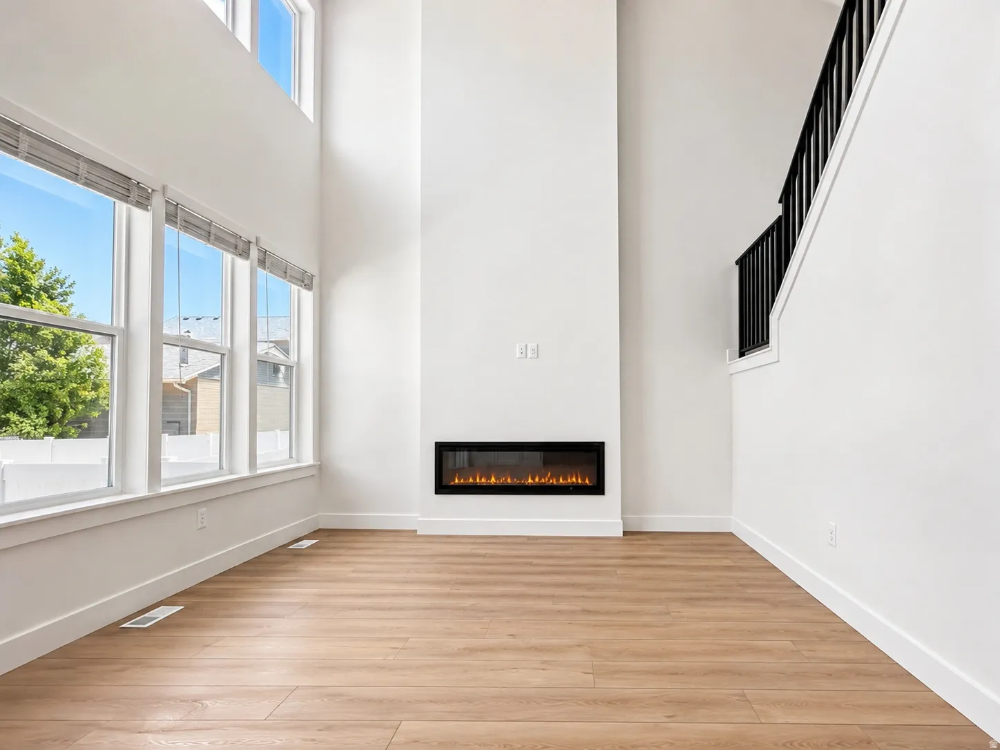 Two-story living area featuring a linear electric fireplace, wood-finish flooring, a contemporary black metal staircase railing, and large windows
