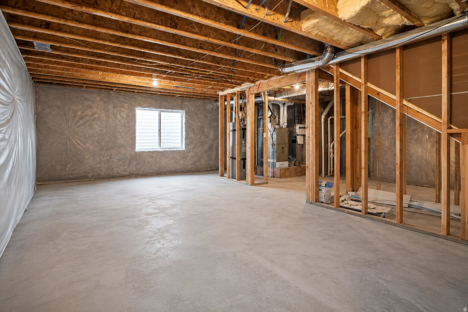 Unfinished basement space featuring exposed wood joists, concrete flooring, and a single window with horizontal blinds