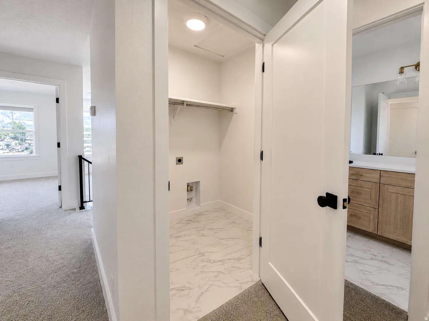 Dedicated utility closet with a built-in shelf and hanging rod, featuring white marble-look flooring