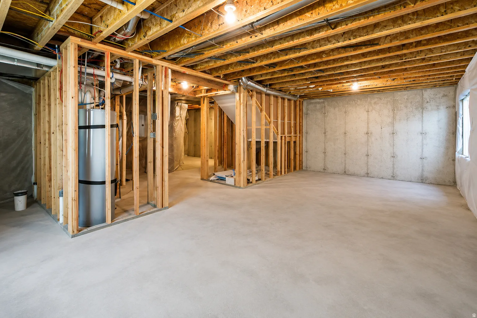 Unfinished basement featuring exposed wood joists, concrete flooring, and framed partitioning