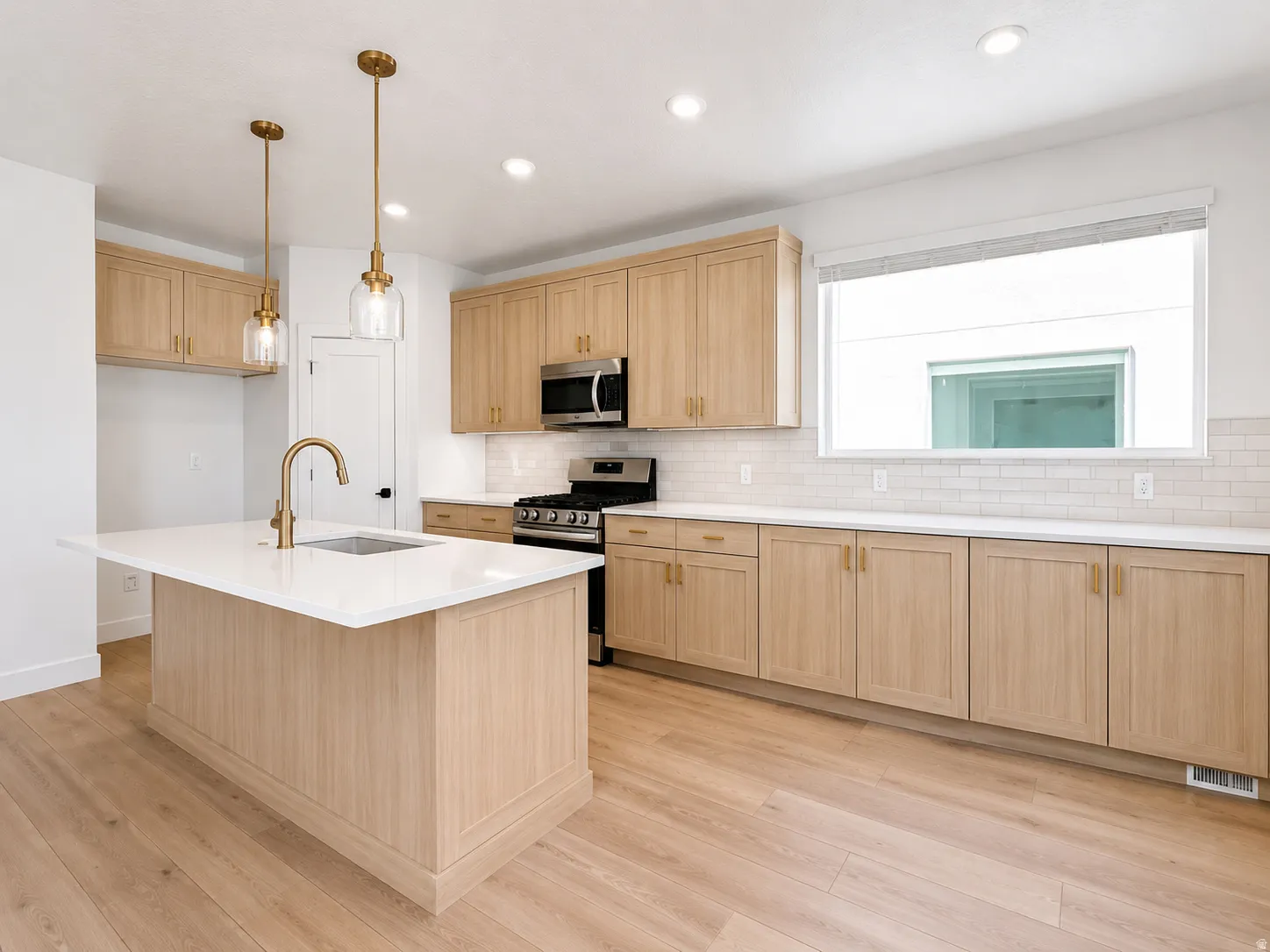 Kitchen featuring light wood-finish cabinetry, a central island with a sink and brass-finish faucet, recessed lighting, and subway tile backsplash