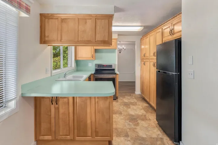 Kitchen featuring wood-finish cabinetry, light green countertops, and a black refrigerator