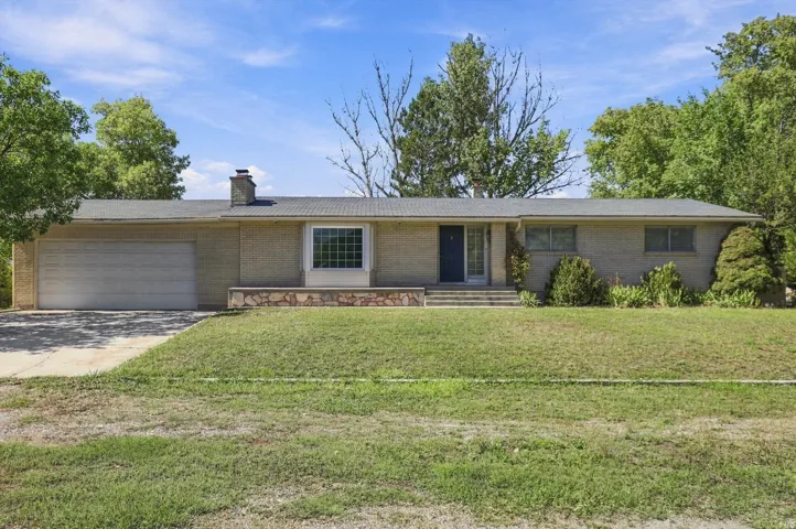 Brick exterior, attached garage, front yard with mature trees, stone-finish planter, and multiple windows