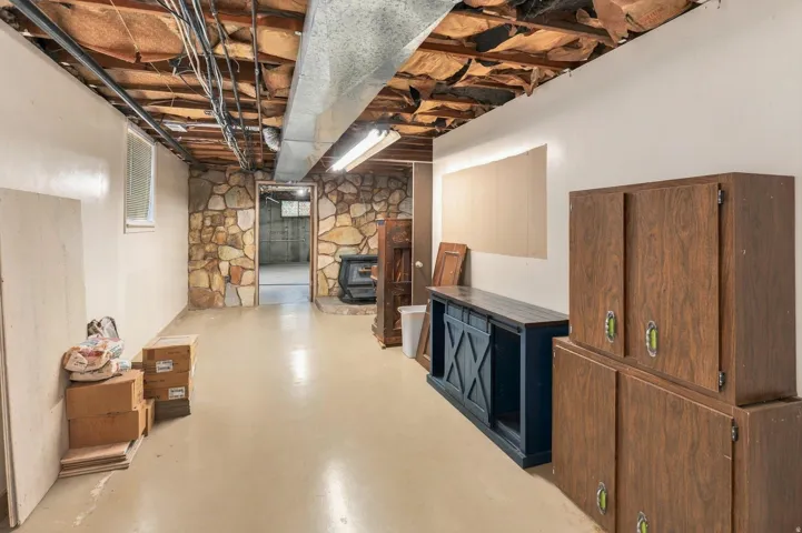 Finished lower level with stone accent wall, light-toned flooring, and exposed ceiling joists
