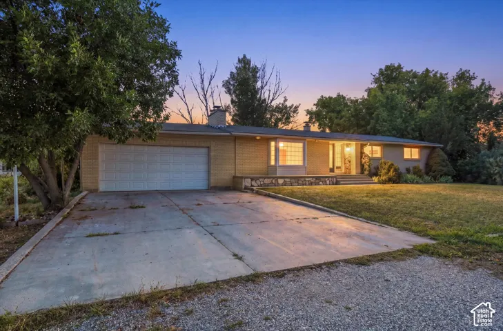 Ranch-style exterior featuring a light-toned brick facade, an attached two-car garage, a concrete driveway, and a front lawn