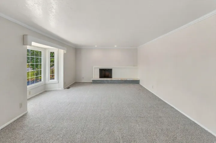 Bay window, fireplace with white mantel, light-colored carpeting, white crown molding, recessed lighting