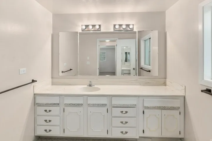 White vanity with multiple storage drawers and cabinet doors, an integrated sink, a light-toned countertop, and a wall-mounted tri-fold mirror