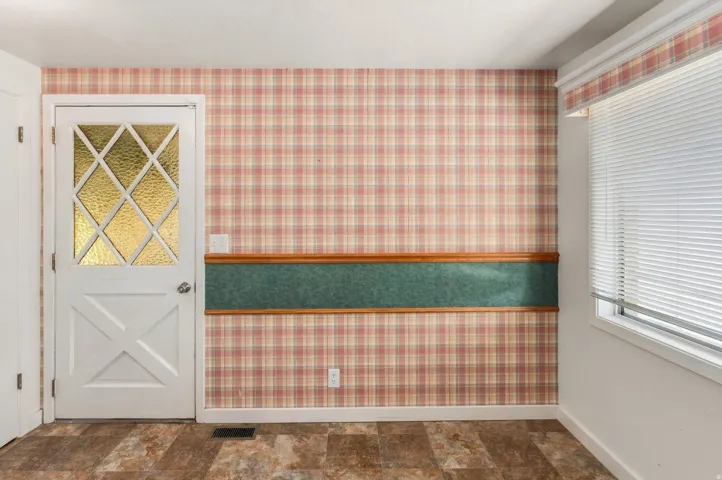 White door with decorative glass inserts, plaid wallpaper, wood-finish flooring, and a window with horizontal blinds