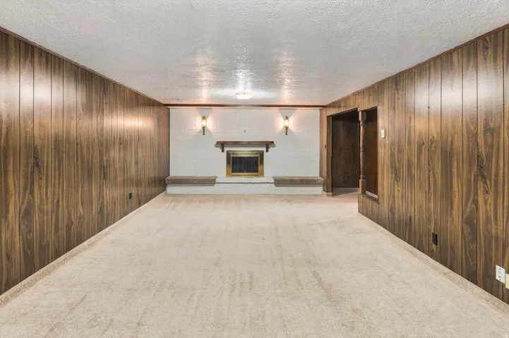 Carpeted room featuring wood-finish wall panels and a white brick fireplace with a wood mantel