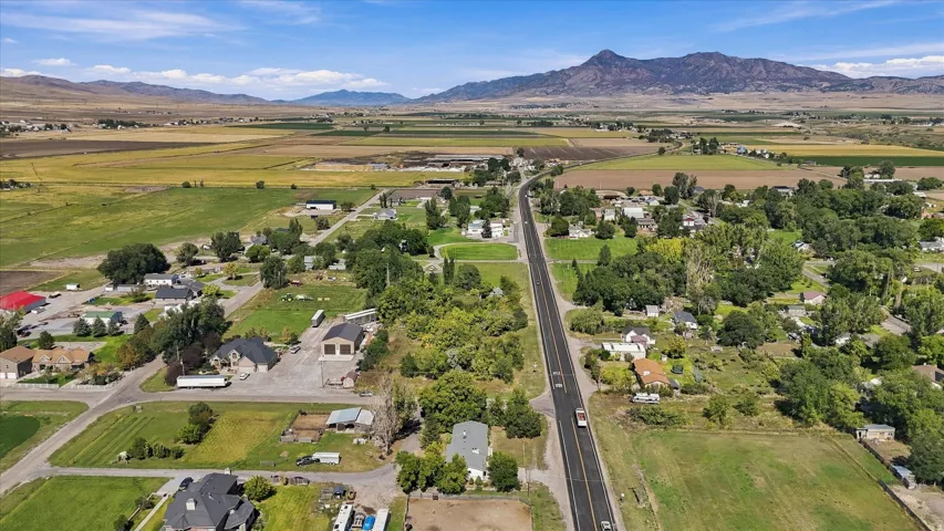 Expansive rural landscape with a paved road, scattered residential structures, mature trees, and agricultural fields