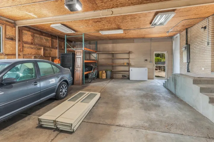 Concrete flooring in garage featuring exposed wood ceiling, fluorescent lighting, and a utility door