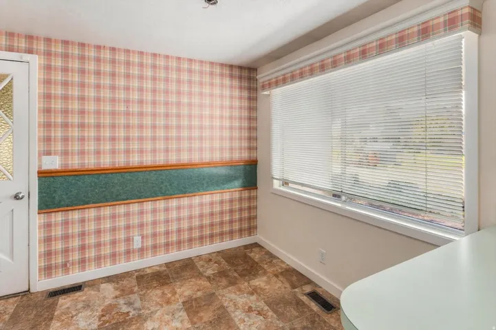 Window with horizontal blinds, patterned wall covering, wood-finish flooring, and a white door with decorative glass