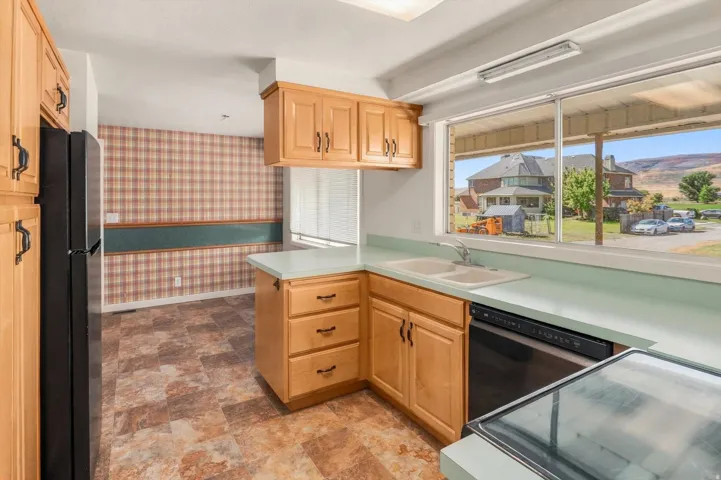 Light wood-finish cabinetry, corner sink, and a black built-in dishwasher