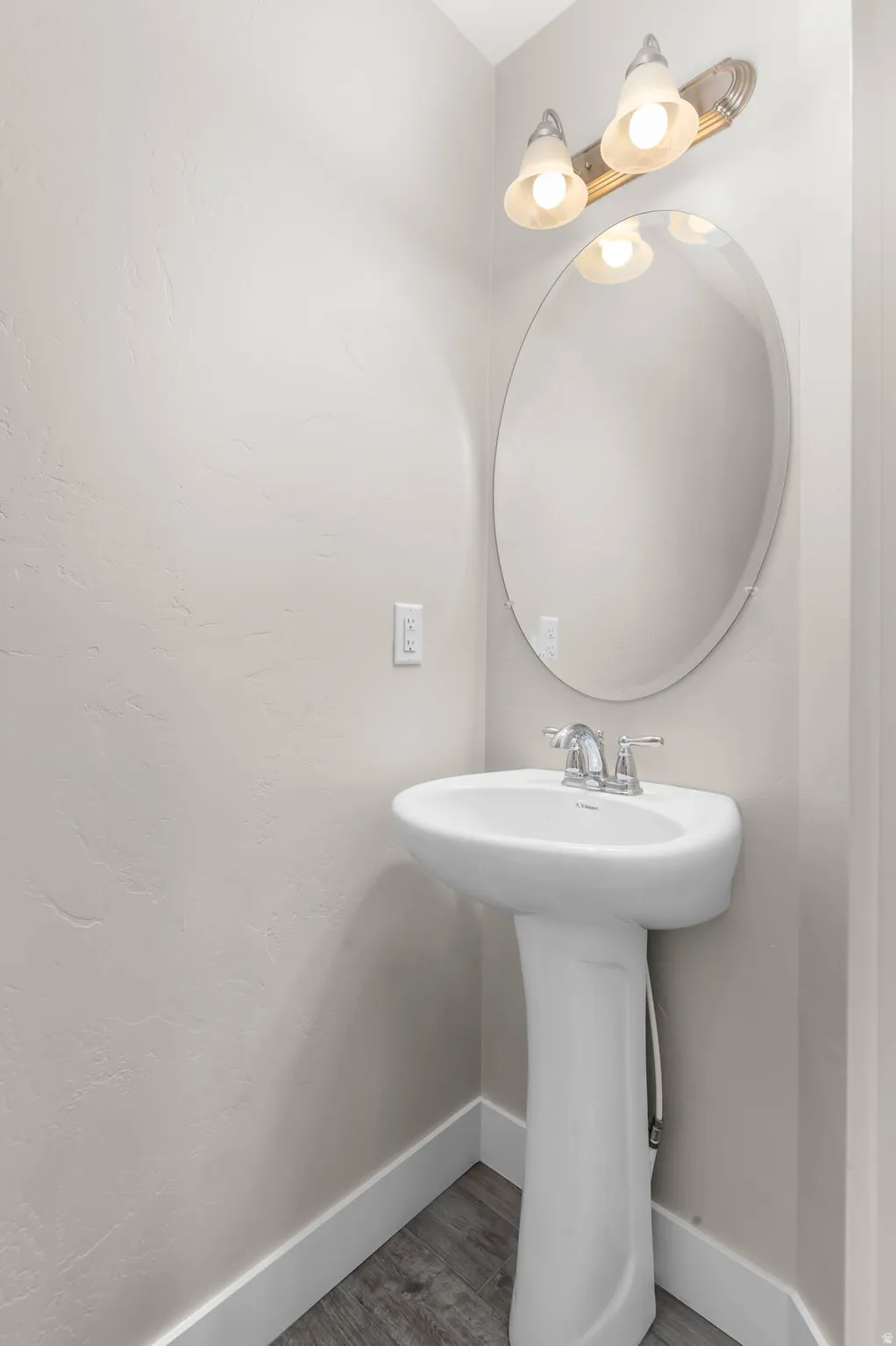 Pedestal sink with chrome fixtures, oval mirror, and a vanity light fixture above