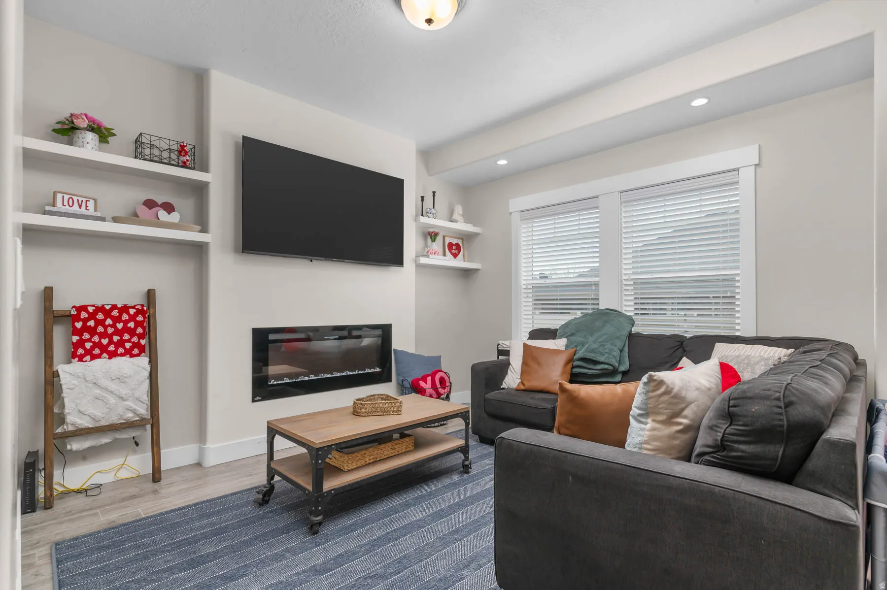 Built-in shelving, mounted fireplace, recessed lighting, wood-finish flooring, and window blinds