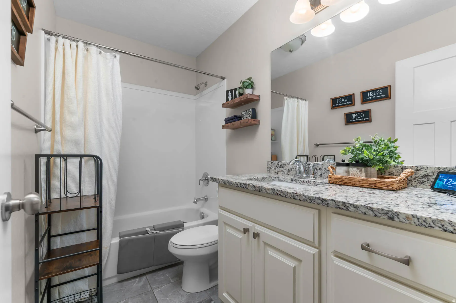 White panel cabinetry with brushed nickel hardware, expansive countertop, large vanity mirror, and white tub/shower combination