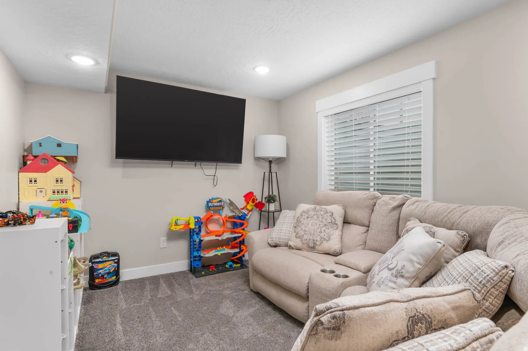 Carpeted flooring, recessed ceiling lighting, wall-mounted television, and a window with blinds
