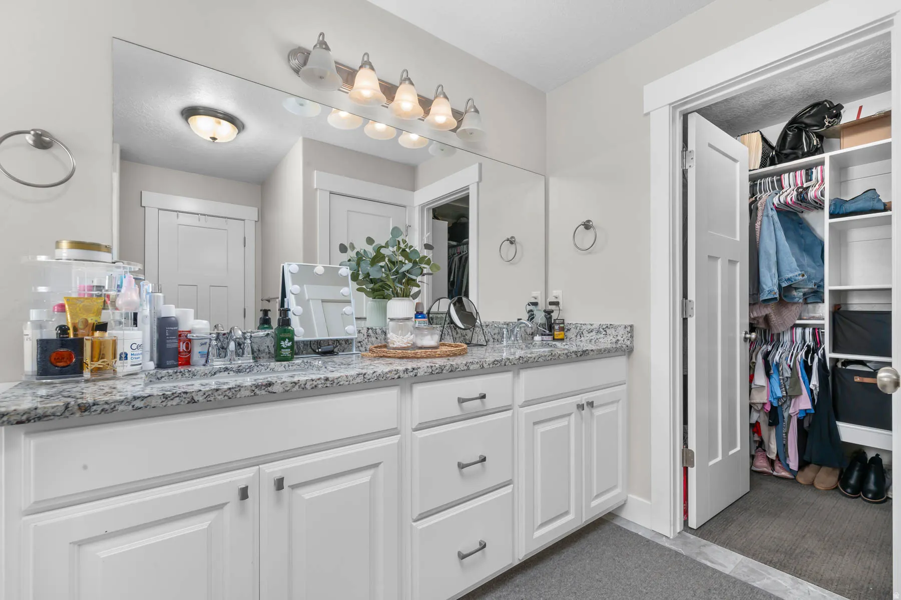 Double vanity with stone countertop, white shaker cabinetry, and an integrated full-width mirror