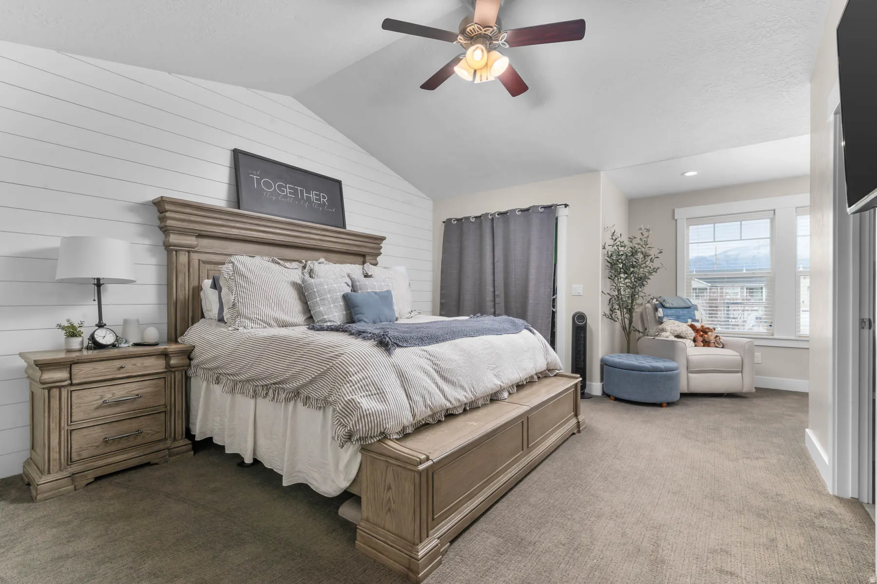 Vaulted ceiling with a ceiling fan, white shiplap accent wall, neutral-toned carpeting, and a window with mountain scenery