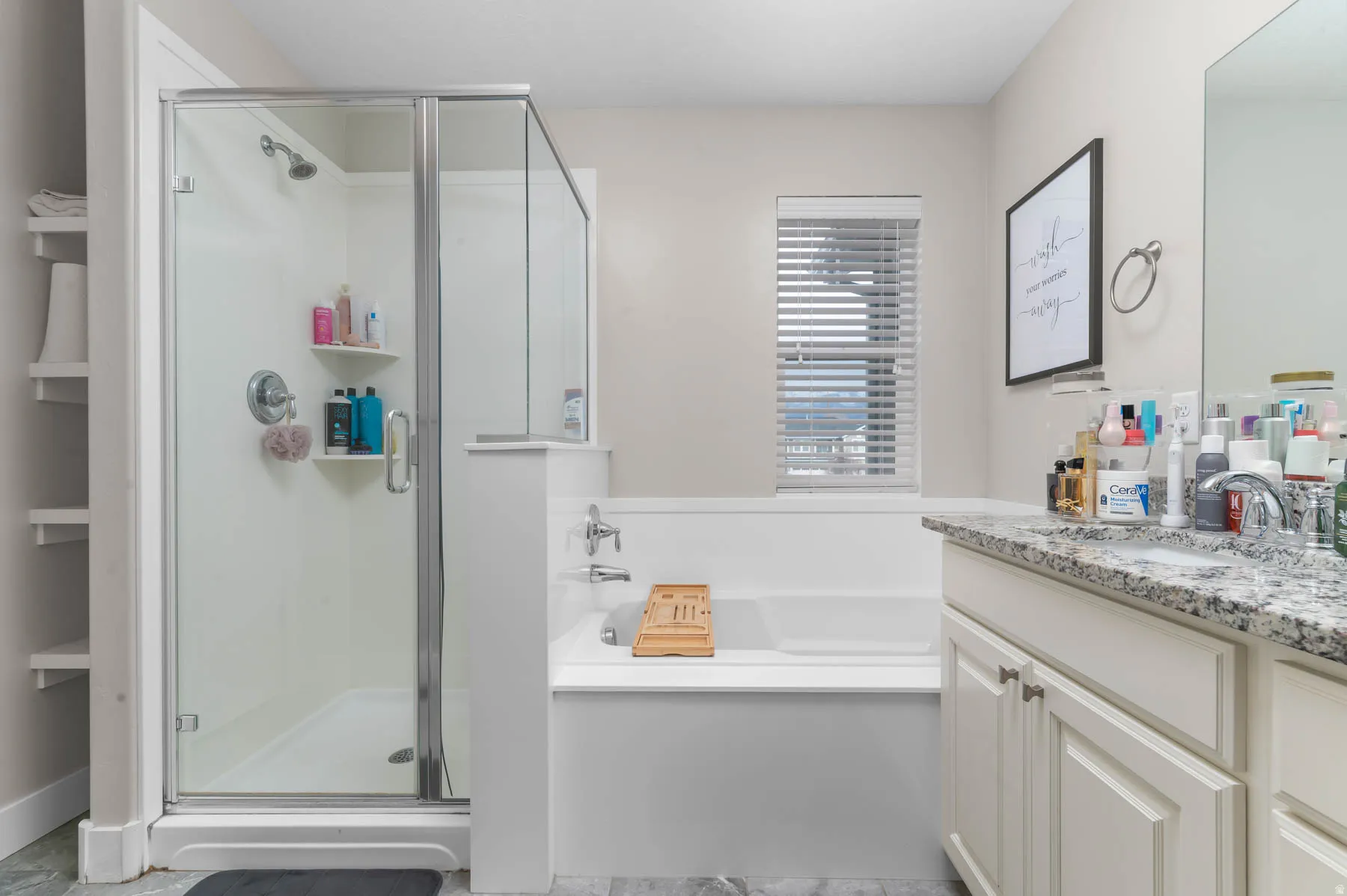 Shower with glass enclosure, built-in bathtub, vanity with stone countertop, and window with blinds