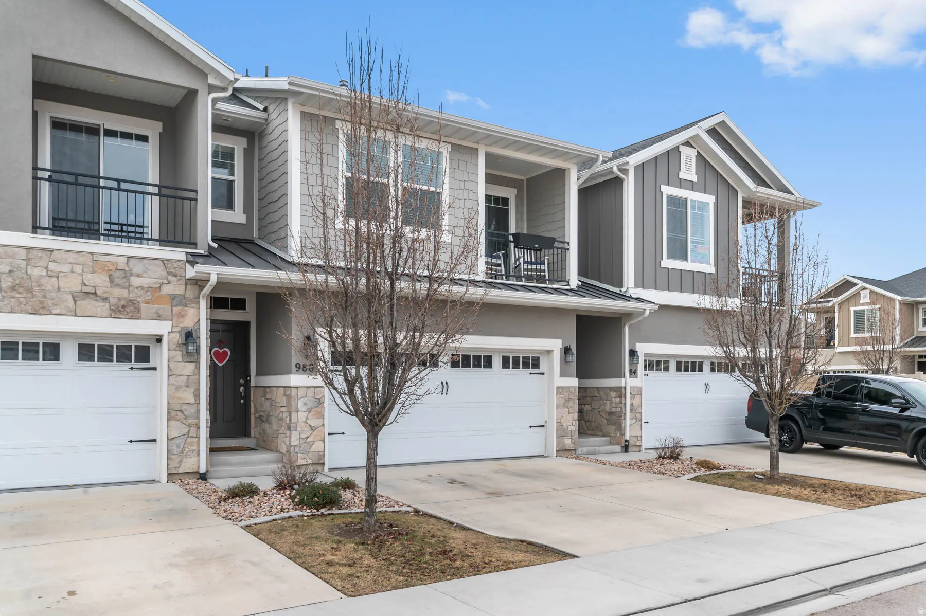 Exterior featuring stone accents, white garage doors, a covered entry, and an upper-level balcony with a black railing