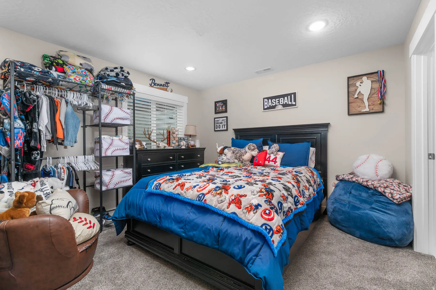 Recessed lighting illuminates the carpeted room, featuring a dark wood-finish bed frame, a coordinating dresser, and a window with blinds
