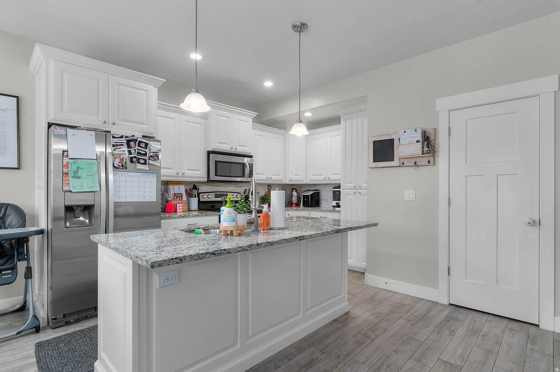 Kitchen featuring white cabinetry, stainless steel appliances, a granite-finish island, two pendant lights, and wood-finish flooring
