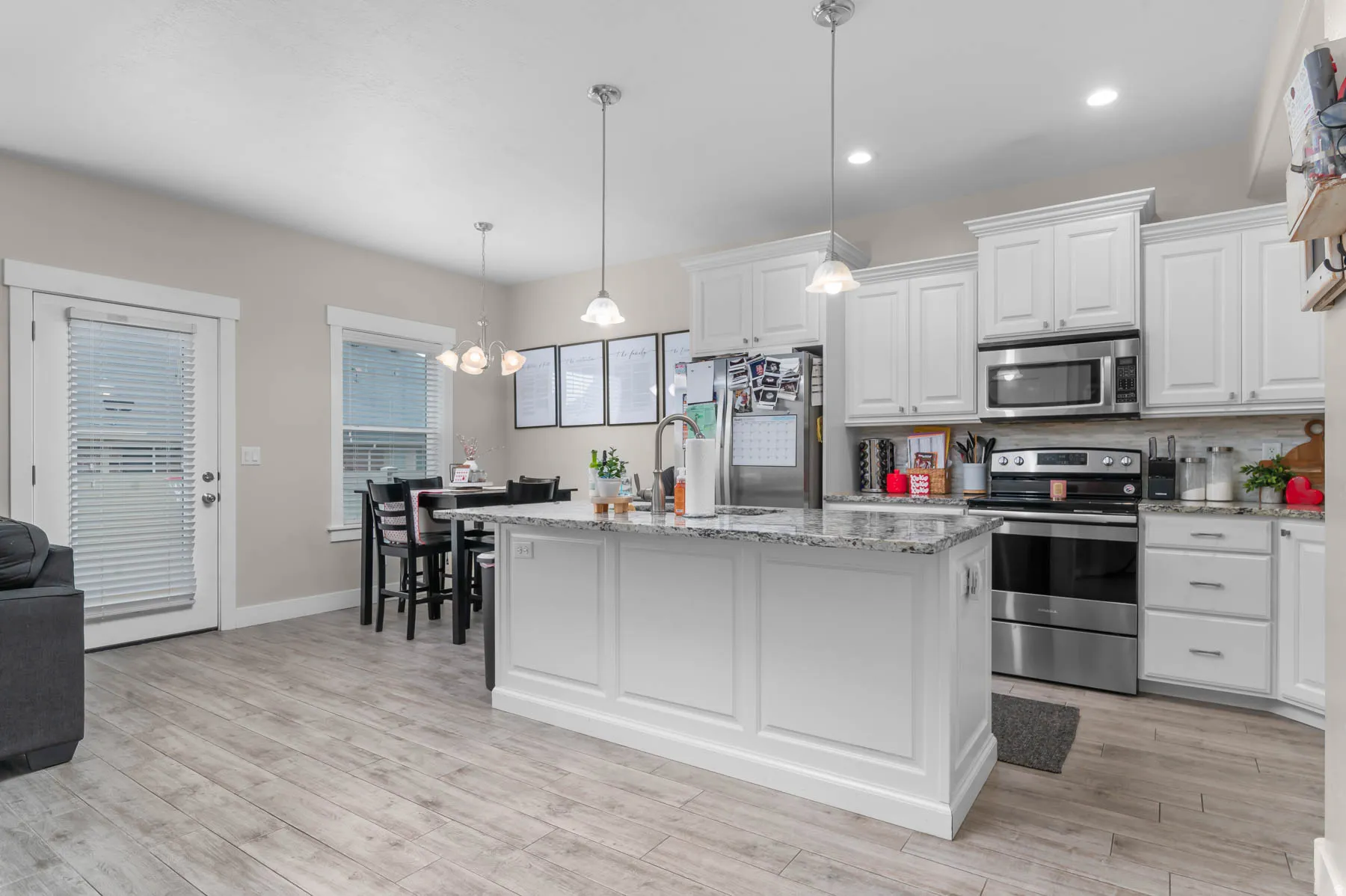 White cabinetry, stainless steel appliances, granite countertops, wood-finish flooring, and recessed lighting