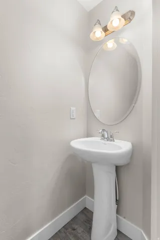 Pedestal sink with chrome fixtures, oval mirror, and a vanity light fixture above