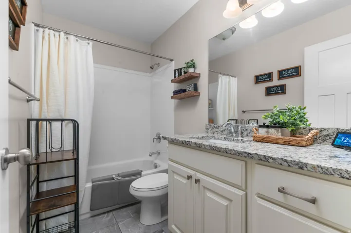 White panel cabinetry with brushed nickel hardware, expansive countertop, large vanity mirror, and white tub/shower combination